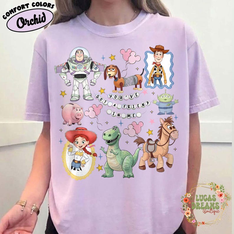 May include: Orchid Comfort Colors t-shirt featuring cartoon characters from the Toy Story movie. The design includes Buzz Lightyear, Woody, Jessie, and other characters, with the phrase "You've Got a Friend in Me."