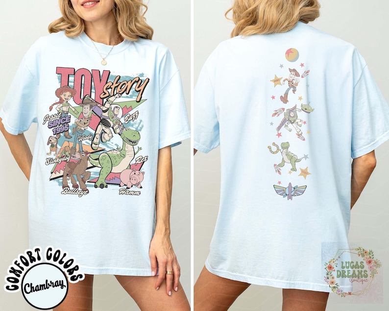 May include: Light blue t-shirt featuring the words "Toy Story" in pink and yellow, with various cartoon characters. The back of the shirt has a vertical design of characters and stars. The shirt is a comfortable, casual style.