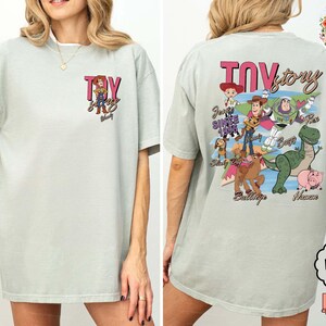 Peut inclure: T-shirt vert clair avec l'inscription "Toy Story" en rose et noir, et un dessin de Woody sur le devant. Le dos du t-shirt pr&eacute;sente divers personnages de Toy Story, dont Buzz l'&Eacute;clair et Rex.