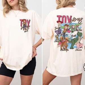 Peut inclure: T-shirt de couleur cr&egrave;me avec une poche avant orn&eacute;e du texte "TOY" et d'une image de personnage de dessin anim&eacute;. Le dos du t-shirt affiche les mots "TOY STORY" et divers personnages de dessins anim&eacute;s. Le t-shirt a une coupe ample et confortable.