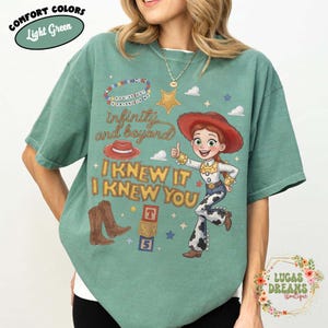 May include: A light green t-shirt featuring a graphic of a cowgirl character, a red cowboy hat, brown cowboy boots, and alphabet blocks. The text reads "YOU'VE GOT A FRIEND IN ME", "infinity and beyond", "I KNEW IT", and "I KNEW YOU" in various fonts.