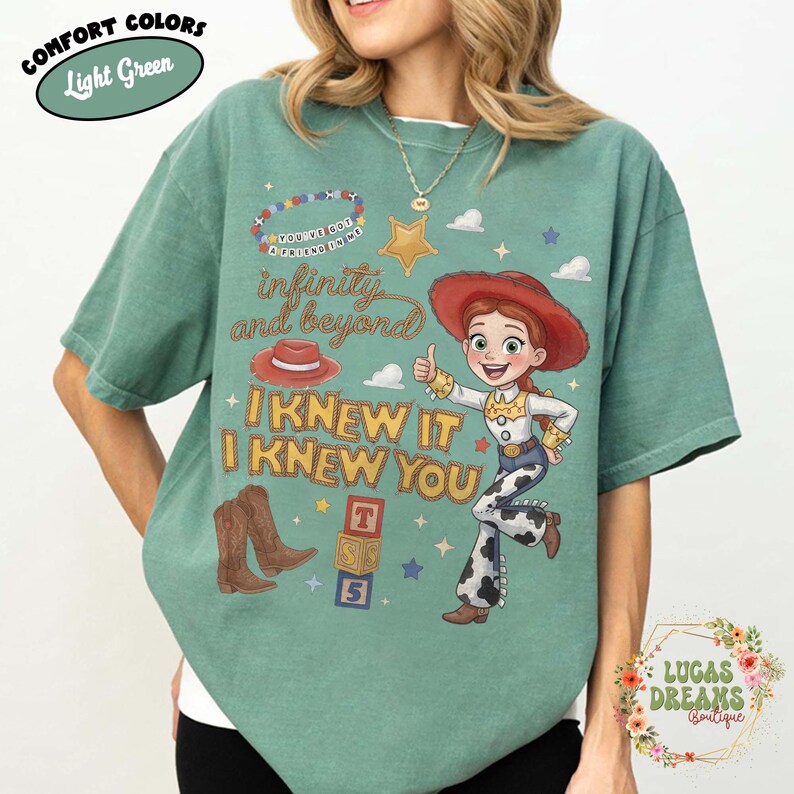 May include: A light green t-shirt featuring a graphic of a cowgirl character, a red cowboy hat, brown cowboy boots, and alphabet blocks. The text reads "YOU'VE GOT A FRIEND IN ME", "infinity and beyond", "I KNEW IT", and "I KNEW YOU" in various fonts.
