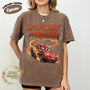 May include: Brown t-shirt featuring Lightning McQueen from the Cars movie. The design includes the text "Lightning McQueen" in red and yellow, with a graphic of the character racing. The shirt has the text "Comfort Colors Espresso" in a circle.