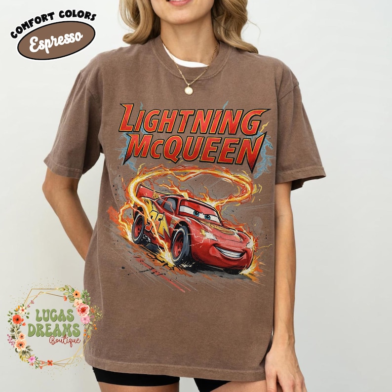May include: Brown t-shirt featuring Lightning McQueen from the Cars movie. The design includes the text "Lightning McQueen" in red and yellow, with a graphic of the character racing. The shirt has the text "Comfort Colors Espresso" in a circle.