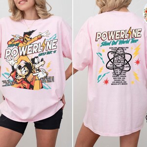 Puede incluir: Camiseta rosa claro con dise&ntilde;o de Powerline. La parte delantera muestra personajes de dibujos animados y el texto "POWERLINE" y "World Tour '95". La parte trasera presenta una lista de ciudades de la gira mundial.