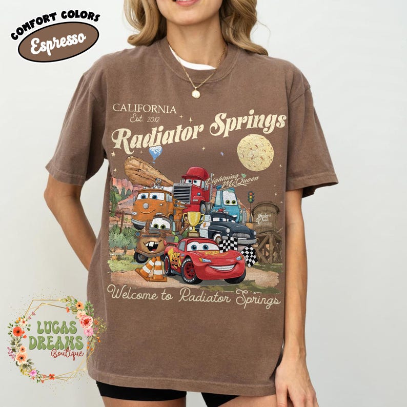 Pode incluir: Camiseta marrom com um gr&aacute;fico de personagens do filme Carros, incluindo Rel&acirc;mpago McQueen. A camisa tem o texto "Radiator Springs" e "Welcome to Radiator Springs". A camisa tamb&eacute;m tem o texto "Comfort Colors Espresso".