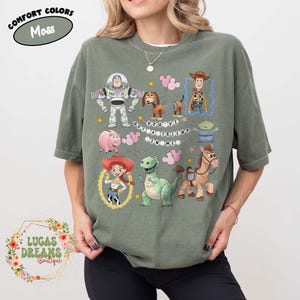 May include: Moss green t-shirt featuring cartoon characters from the movie Toy Story. The shirt has Buzz Lightyear, Woody, Jessie, and other characters. The text "YOU'VE GOT A FRIEND IN ME" is also on the shirt.
