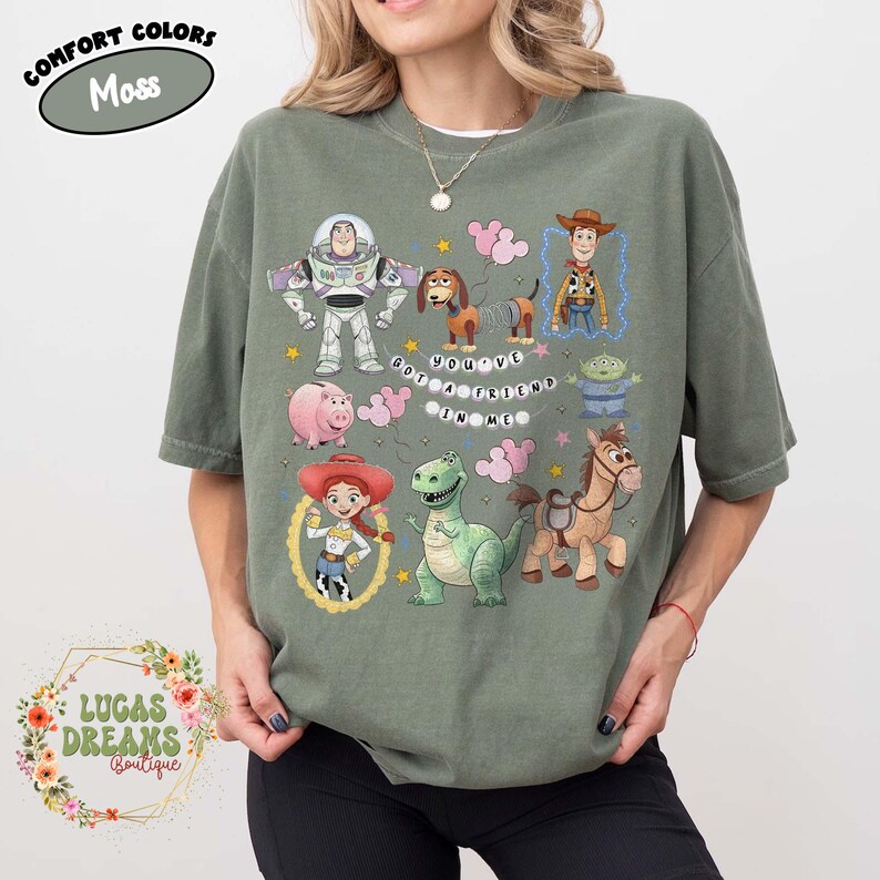 May include: Moss green t-shirt featuring cartoon characters from the movie Toy Story. The shirt has Buzz Lightyear, Woody, Jessie, and other characters. The text "YOU'VE GOT A FRIEND IN ME" is also on the shirt.