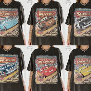 May include: Six dark gray t-shirts featuring different characters from the movie Cars. Each shirt has a vintage-style graphic with the character's name and a racing theme. The shirts are oversized.