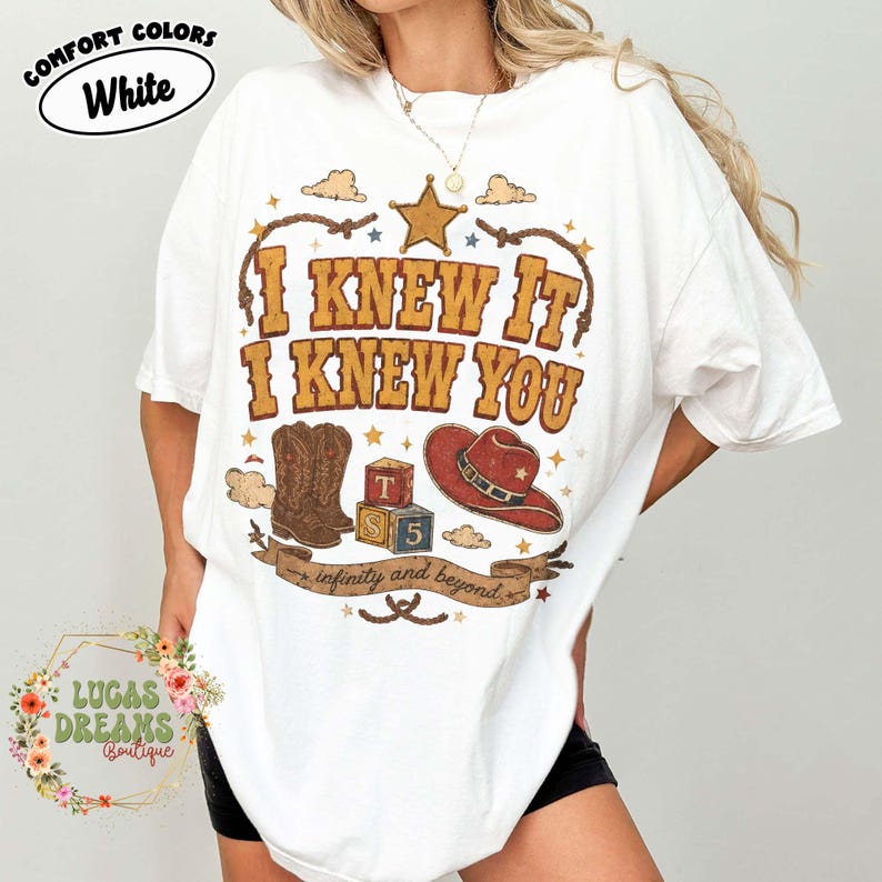 May include: A white t-shirt featuring a graphic print with the text I KNEW IT I KNEW YOU, a brown cowboy boot, a red cowboy hat, two alphabet blocks labelled T and S, and a banner with the text infinity and beyond, all framed by a lasso.