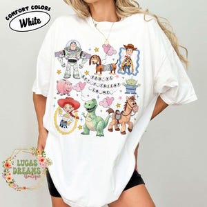 May include: White t-shirt featuring colorful cartoon characters from a popular animated movie. The shirt includes the text "YOU'VE GOT A FRIEND IN ME" and the words "COMFORT COLORS White". The shirt is from Lucas Dreams Boutique.