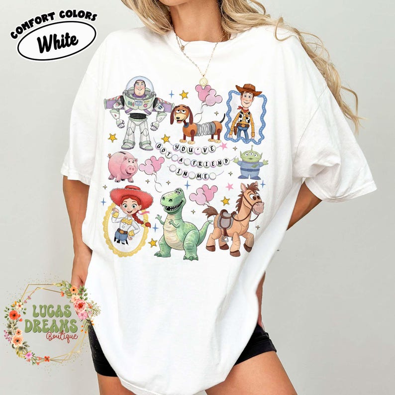 May include: White t-shirt featuring colorful cartoon characters from a popular animated movie. The shirt includes the text "YOU'VE GOT A FRIEND IN ME" and the words "COMFORT COLORS White". The shirt is from Lucas Dreams Boutique.