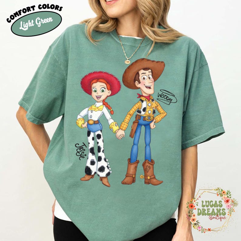 Puede incluir: Camiseta verde claro con una ilustraci&oacute;n de dibujos animados de Jessie y Woody de Toy Story. Jessie lleva un sombrero rojo, una camisa blanca y pantalones con estampado de vaca. Woody lleva un sombrero de vaquero, una camisa amarilla y pantalones azules. La camiseta tiene el texto "Comfort Colors Light Green".
