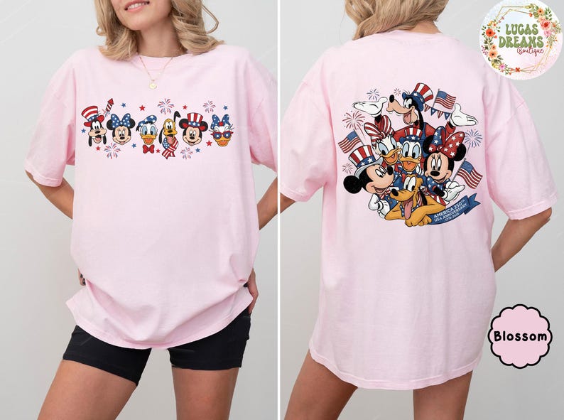 以下が含まれることがあります： 愛国的な漫画のデザインが施された、明るいピンク色のTシャツ。前面には、お祝いの帽子と花火をかぶった漫画のキャラクターが描かれています。Tシャツの背面には、アメリカの国旗と花火を持ったキャラクターのグループが描かれています。