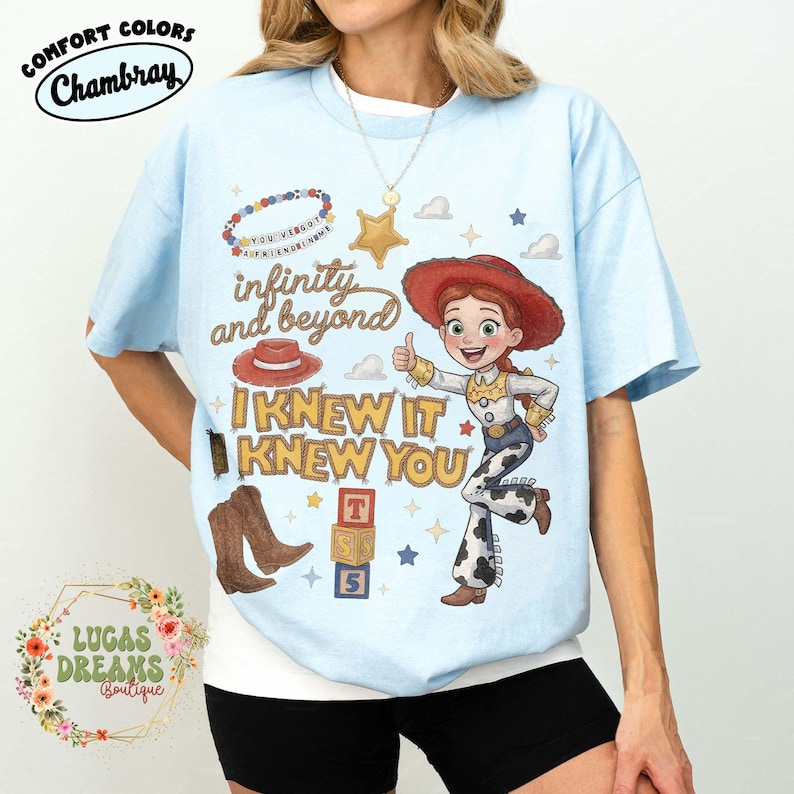 May include: A light blue t-shirt featuring a graphic print of a cowgirl character, a red cowboy hat, brown boots, alphabet blocks, and a beaded necklace. The text reads "infinity and beyond" and "I KNEW IT KNEW YOU" in stylized yellow and brown lettering.