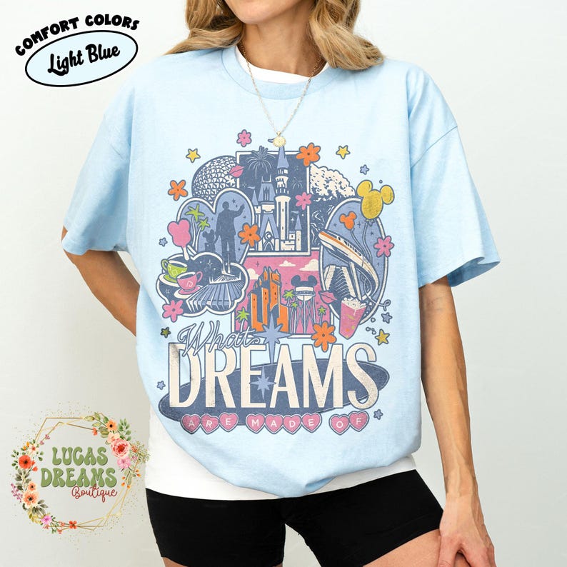 K&ouml;nnte beinhalten: Hellblaues T-Shirt mit einem farbenfrohen Grafikdesign mit einem Schloss, einer Einschienenbahn und dem Text "What Dreams Are Made Of". Das Shirt hat auch den Text "Comfort Colors" und "Light Blue" in einem Kreis.
