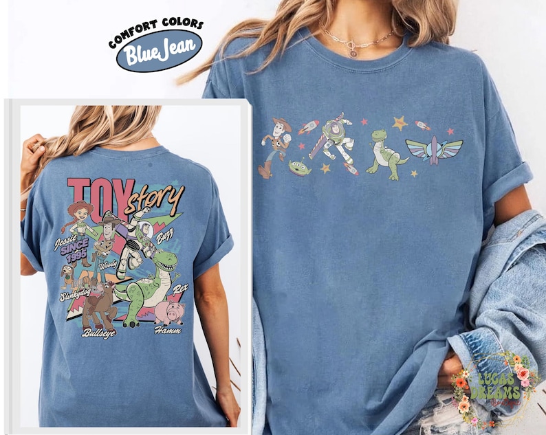May include: Blue jean Comfort Colors t-shirt featuring Toy Story characters. The front displays a line of characters including Woody and Buzz Lightyear. The back of the shirt has the Toy Story logo and other characters like Jessie and Rex.