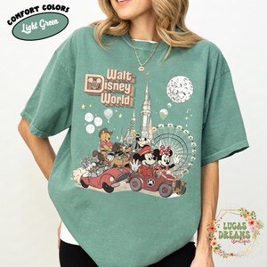 May include: Light green t-shirt with a graphic of Disney characters in cars, the text "Walt Disney World", and a Ferris wheel. The shirt also has the text "Comfort Colors" and "Light Green" in a circle.