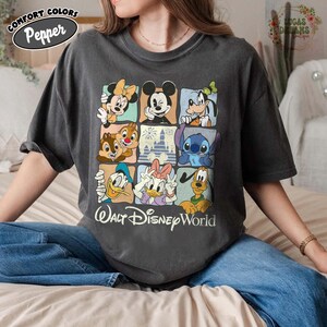 K&ouml;nnte beinhalten: Dunkelgraues Comfort Colors T-Shirt mit einem Raster von Disney-Figuren, darunter Micky Maus, Minnie Maus und Stitch. Das Shirt tr&auml;gt den Schriftzug "Walt Disney World" darunter. Das T-Shirt hat eine lockere Passform.