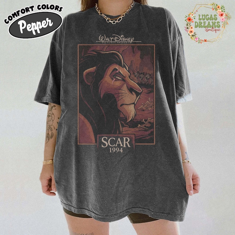 May include: A charcoal grey short-sleeve t-shirt featuring a graphic print of the character Scar from The Lion King. The design includes the text Walt Disney Pictures Presents, Scar, and 1994. The shirt has a crew neckline and a relaxed fit.
