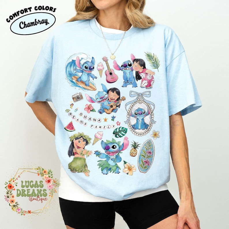 May include: Light blue t-shirt featuring a collage of cartoon characters. The design includes images of a blue alien-like creature surfing, playing a guitar, and interacting with a girl. The text "OHANA MEANS FAMILY" is also present.