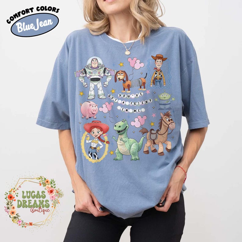May include: Blue t-shirt with a graphic of characters from the animated movie Toy Story. The shirt features Buzz Lightyear, Woody, Jessie, Rex, Hamm, Slinky Dog, Bullseye, and the Little Green Men. Text on the shirt reads "You've Got a Friend in Me."