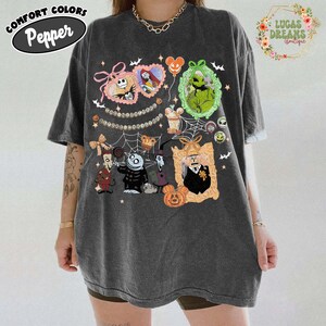 Puede incluir: Camiseta gris oscuro con personajes de dibujos animados en marcos ornamentados, incluyendo Jack Skellington y Sally. La camiseta tiene las palabras "Comfort Colors Pepper" en un &oacute;valo negro y "Lucas Dreams Boutique" en una corona floral.