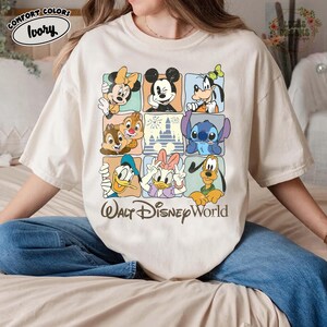 K&ouml;nnte beinhalten: Elfenbeinfarbenes T-Shirt mit einem Raster von Disney-Figuren, darunter Micky Maus, Minnie Maus, Donald Duck und Stitch. Die Worte "Walt Disney World" sind unter dem Raster aufgedruckt. Das Shirt hat auch die Worte "Comfort Colors" und "Ivory" auf der oberen linken Seite.