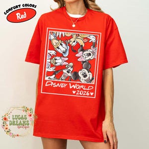 Op de afbeelding: Rood T-shirt met een Disney World 2026-afbeelding met Mickey Mouse, Minnie Mouse, Donald Duck, Goofy en andere personages. Het shirt heeft een Comfort Colors-label.