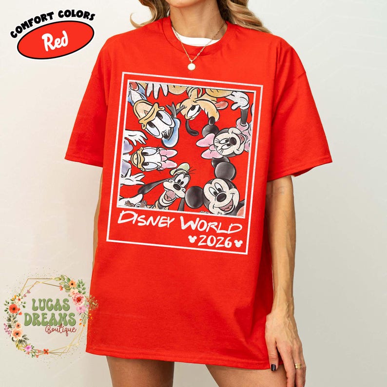 Op de afbeelding: Rood T-shirt met een Disney World 2026-afbeelding met Mickey Mouse, Minnie Mouse, Donald Duck, Goofy en andere personages. Het shirt heeft een Comfort Colors-label.