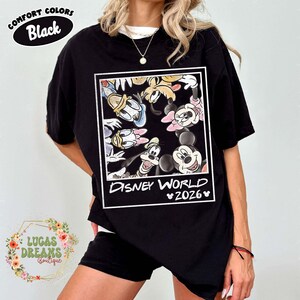 Op de afbeelding: Zwart T-shirt met een Disney World 2026-afbeelding met Mickey en Minnie Mouse, Donald en Daisy Duck, Goofy en Pluto. Het shirt heeft bovenaan de tekst "Comfort Colors Black".