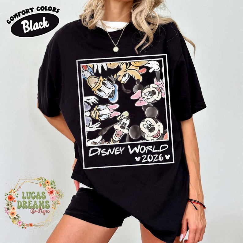 Op de afbeelding: Zwart T-shirt met een Disney World 2026-afbeelding met Mickey en Minnie Mouse, Donald en Daisy Duck, Goofy en Pluto. Het shirt heeft bovenaan de tekst "Comfort Colors Black".