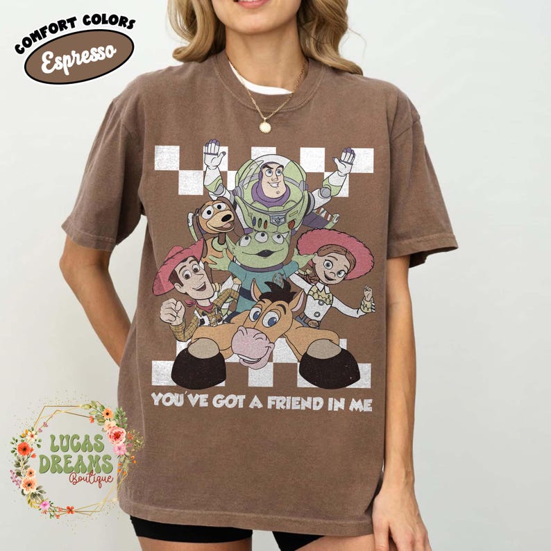 以下が含まれることがあります： エスプレッソブラウンの半袖Tシャツ。ウッディ、バズ・ライトイヤー、ジェシー、ブルズアイ、エイリアンといったトイ・ストーリーのキャラクターのグラフィックプリントが施されています。キャラクターの下には「YOU'VE GOT A FRIEND IN ME」というテキストが白でプリントされています。