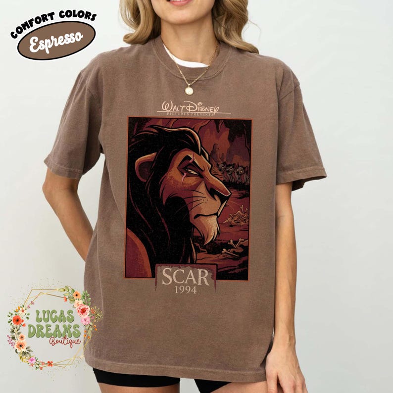 May include: A brown short-sleeve t-shirt featuring a graphic print of the character Scar from The Lion King. The design includes the text Walt Disney Pictures Presents, Scar, and 1994. The shirt has a crew neckline and a relaxed, boxy fit.
