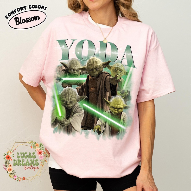 Puede incluir: Una camiseta de manga corta de color rosa claro con un estampado gr&aacute;fico del personaje Yoda en varias poses con sables de luz verdes. La palabra YODA est&aacute; impresa en letras grandes sobre el personaje. Incluye una etiqueta Comfort Colors Blossom.