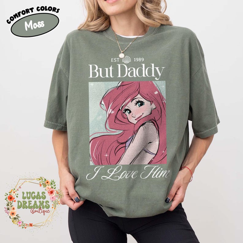 May include: Moss green t-shirt with the text "But Daddy I Love Him" and an illustration of a cartoon character with pink hair. The shirt also has the text "EST 1989" and the words "Comfort Colors" in an oval.