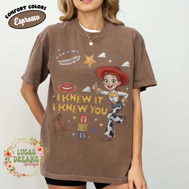 May include: An espresso brown short-sleeve t-shirt featuring a graphic print of a cowgirl character, a red hat, brown boots, and alphabet blocks. The text reads: You've got a friend in me, infinity and beyond, and I KNEW IT I KNEW YOU.