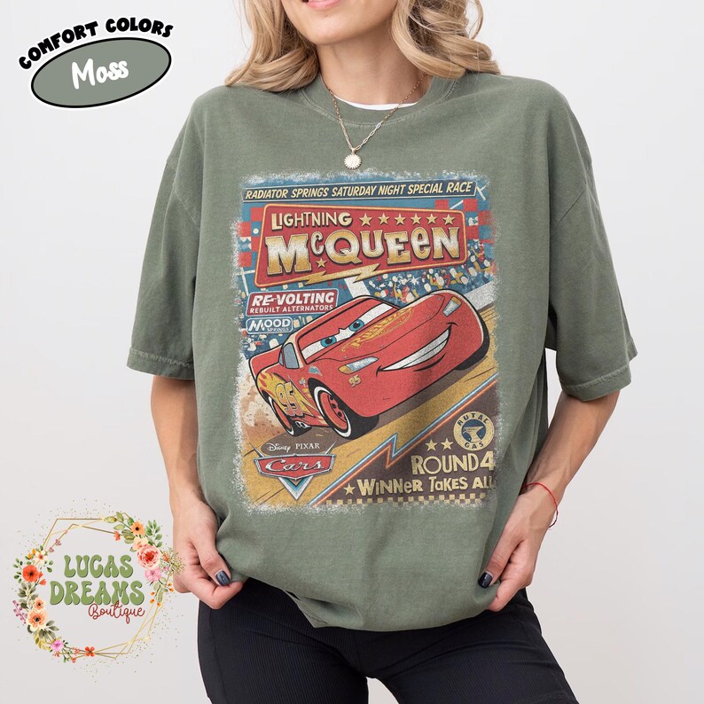 May include: Moss green t-shirt featuring a graphic of Lightning McQueen from the Disney Pixar Cars movie. The design includes the text "Lightning McQueen" and "Round 4 Winner Takes All". The shirt is a comfort colors style.
