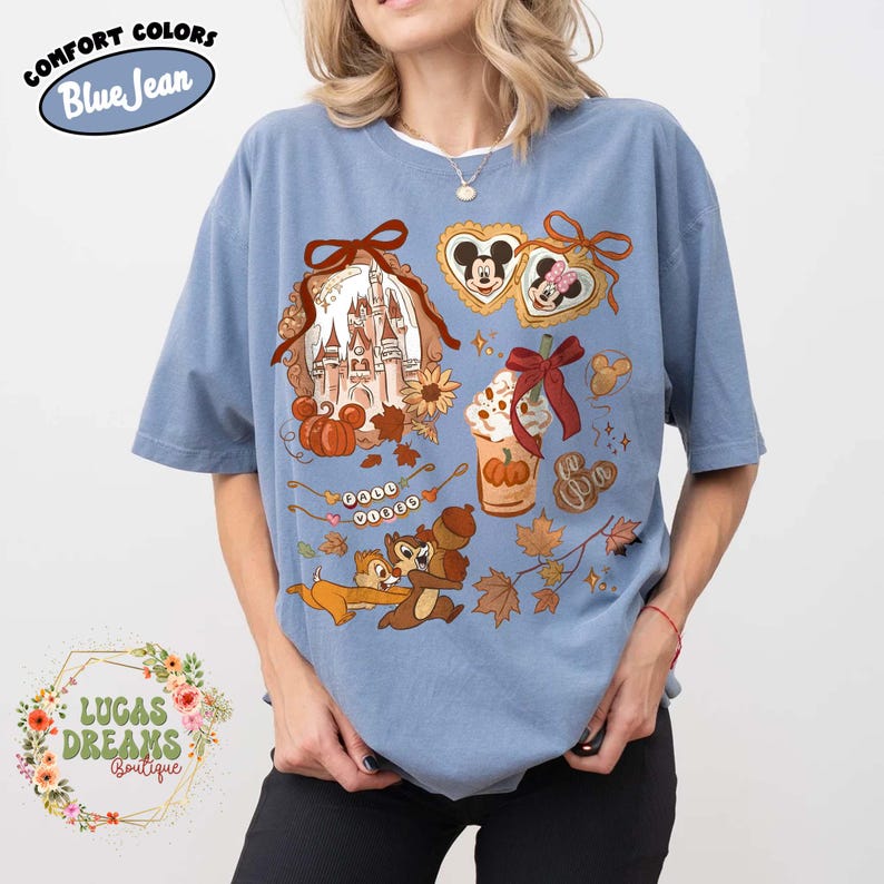 May include: Blue short-sleeve t-shirt with a colorful graphic featuring a castle, pumpkins, Mickey and Minnie Mouse, Chip and Dale, and autumn leaves. The shirt has the text "COMFORT COLORS Blue Jean" and "LUCAS DREAMS Boutique".