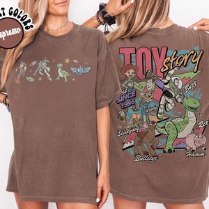 May include: Espresso-coloured t-shirt featuring Toy Story characters. The front displays a line of characters, while the back showcases a larger graphic with the Toy Story logo and more characters. The shirt is a comfort colours style.