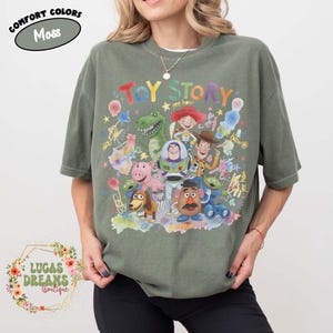 Pu&ograve; includere: T-shirt verde muschio con una grafica colorata dei personaggi di Toy Story. Il design include Woody, Buzz Lightyear, Rex, Jessie e altri personaggi del film d'animazione. Le parole "TOY STORY" sono visualizzate sopra i personaggi.