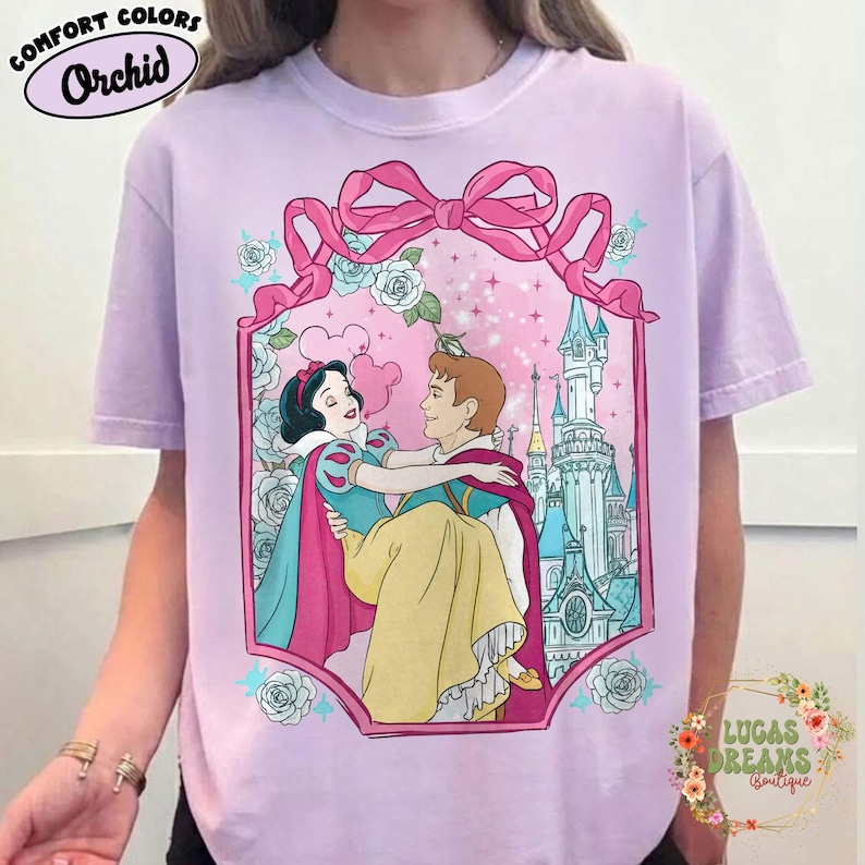 Puede incluir: Camiseta lila Orchid Comfort Colors con una ilustraci&oacute;n enmarcada de Blancanieves y el Pr&iacute;ncipe Encantador. El gr&aacute;fico incluye un lazo rosa, rosas y un castillo. La camiseta tiene el texto "Comfort Colors" y "Orchid" en la parte superior.