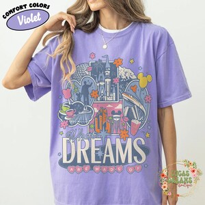 K&ouml;nnte beinhalten: Violettes Comfort Colors T-Shirt mit einem farbenfrohen Grafikdesign. Das Design zeigt ein Schloss, Blumen und den Text "What Dreams Are Made Of". Das T-Shirt hat eine helle violette Farbe.