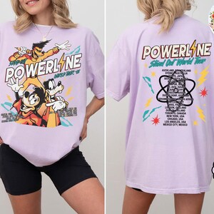 Puede incluir: Una camiseta de color lila con un gr&aacute;fico de los personajes de Powerline. El dise&ntilde;o frontal incluye la palabra "POWERLINE" y personajes de dibujos animados. La parte trasera de la camiseta enumera ciudades del "Stand Out World Tour".