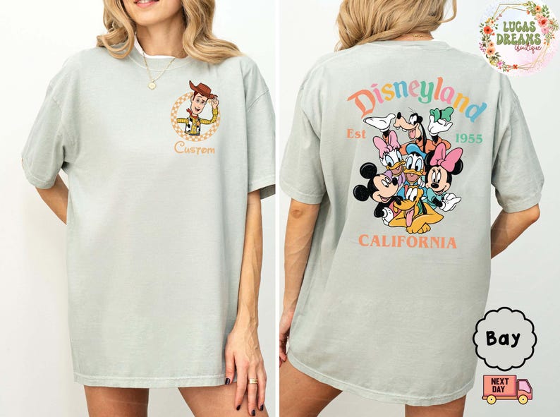 Puede incluir: Camiseta verde claro con un dibujo animado de Woody de Toy Story en la parte delantera y la palabra "Custom" debajo. La parte trasera de la camiseta muestra un gr&aacute;fico de Disneyland con Mickey, Minnie y otros personajes.