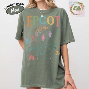 Puede incluir: Camiseta verde musgo con la palabra "EPCOT" en letras coloridas. La camiseta presenta un gr&aacute;fico de la bola EPCOT, personajes de Disney y las palabras "World Tour" y "Since 1982". Parte de la colecci&oacute;n Comfort Colors.
