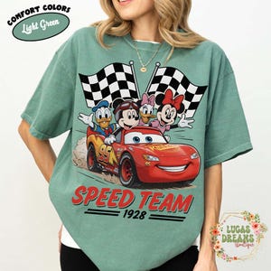 Op de afbeelding: Lichtgroen T-shirt met een rode raceauto met Mickey Mouse, Donald Duck, Daisy Duck en Minnie Mouse. De auto heeft nummer 95 en de woorden "SPEED TEAM 1928". Het shirt heeft ook de woorden "COMFORT COLORS" en "Light Green".