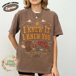 May include: An espresso brown short-sleeve t-shirt featuring a graphic print with the text I KNEW IT I KNEW YOU and infinity and beyond. The design includes a yellow star, a pair of brown cowboy boots, a red cowboy hat, and alphabet blocks.