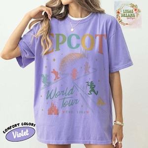 Puede incluir: Camiseta violeta Comfort Colors con gr&aacute;fico "EPCOT World Tour". Presenta un dise&ntilde;o colorido con personajes de dibujos animados, un castillo y el texto "EST. 1982". La camiseta tiene mangas cortas y cuello redondo.