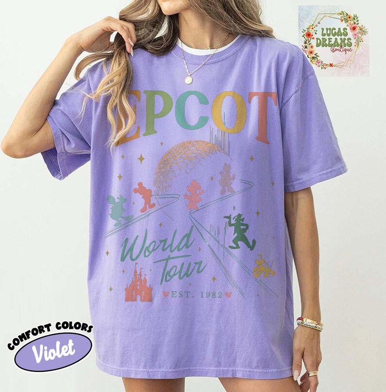 Puede incluir: Camiseta violeta Comfort Colors con gr&aacute;fico "EPCOT World Tour". Presenta un dise&ntilde;o colorido con personajes de dibujos animados, un castillo y el texto "EST. 1982". La camiseta tiene mangas cortas y cuello redondo.